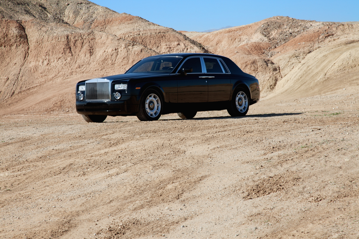 Rolls royce car parked on unpaved road with mountains in background